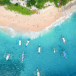 boats approaching a shore with birds-eye view of tiny people