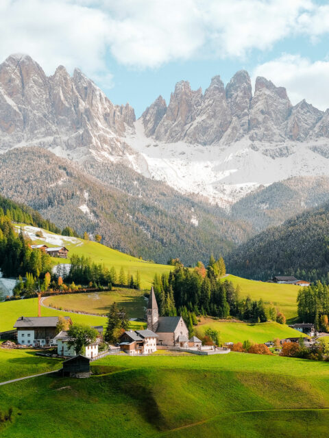 cluster of village homes on green pastures with snowy mountains in the background