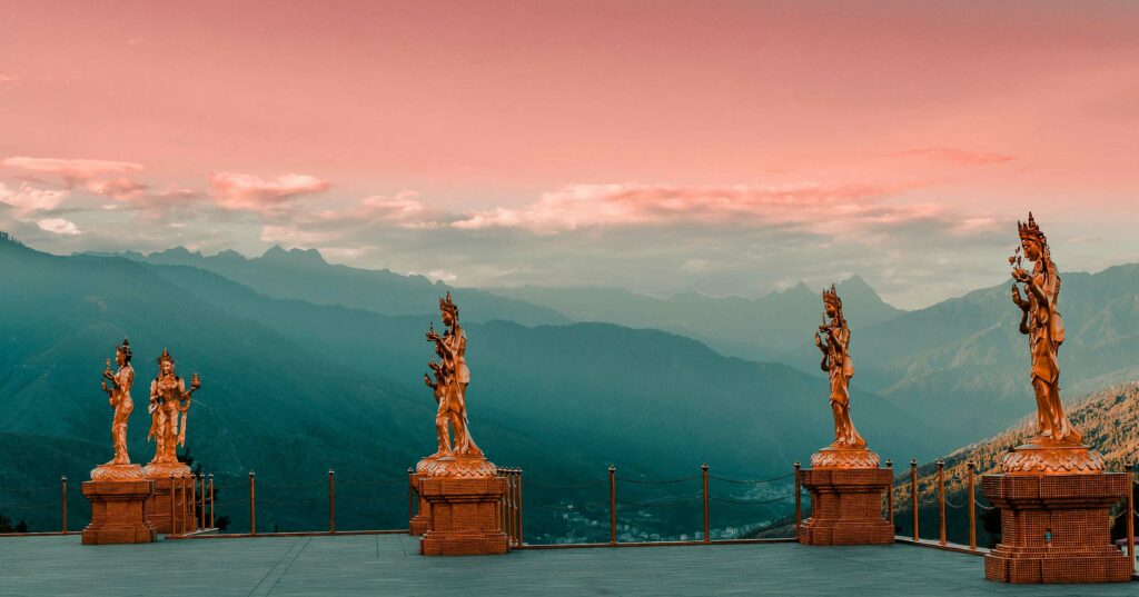 statue of goddesses in bhutan with pink sky and green mountains in the background