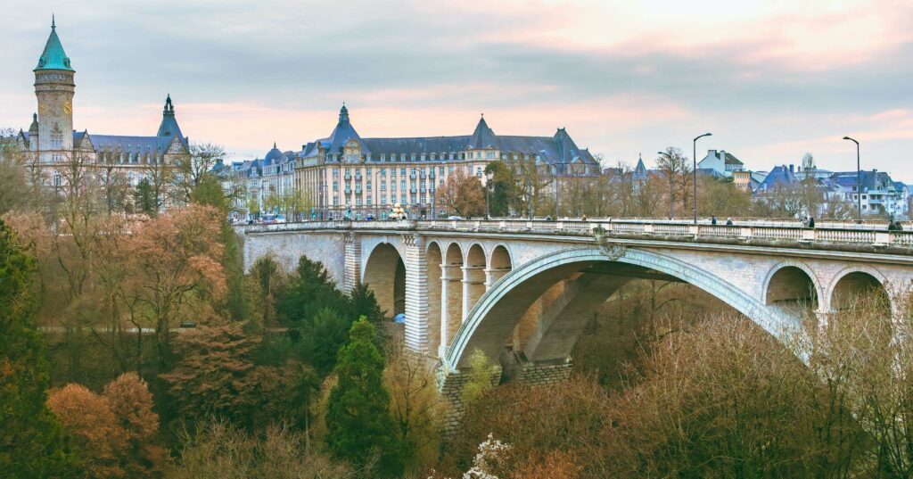 A charming stone bridge with multiple arches leads to an elegant building surrounded by lush greenery