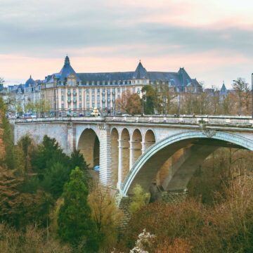 A charming stone bridge with multiple arches leads to an elegant building surrounded by lush greenery