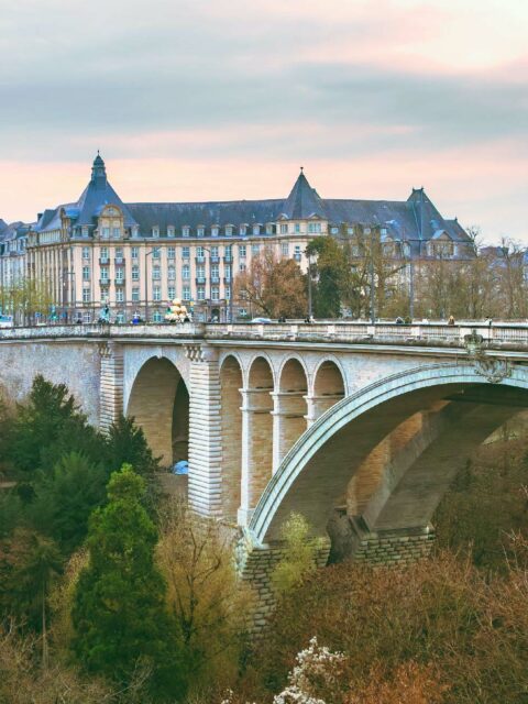 A charming stone bridge with multiple arches leads to an elegant building surrounded by lush greenery