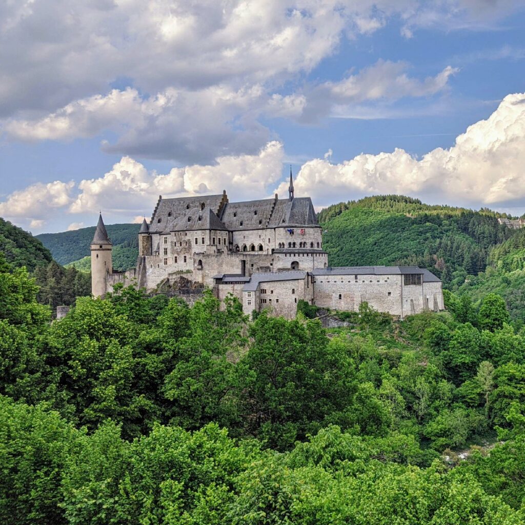 A majestic castle nestled amidst lush greenery, under a sky dotted with fluffy clouds.