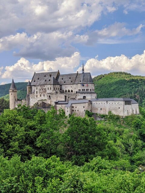 A majestic castle nestled amidst lush greenery, under a sky dotted with fluffy clouds.