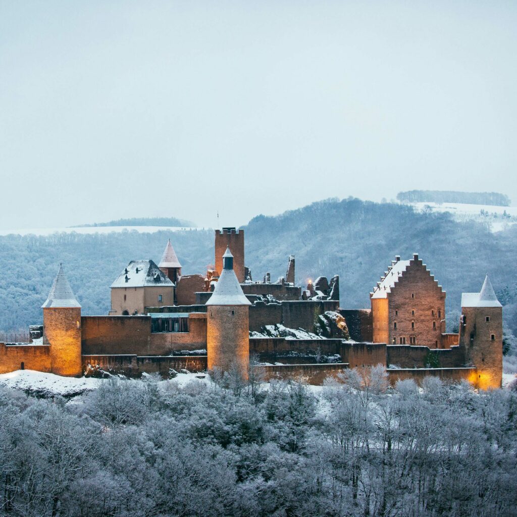 A majestic castle with multiple towers and turrets, surrounded by a snowy landscape and backed by rolling hills