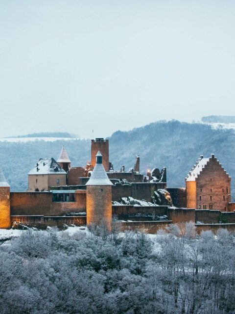 A majestic castle with multiple towers and turrets, surrounded by a snowy landscape and backed by rolling hills