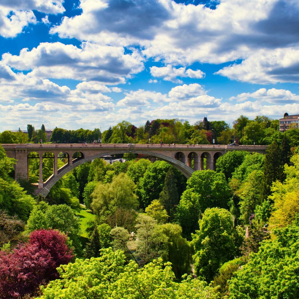 A stone arch bridge, the Pont Adolphe, spans a river gorge in Luxembourg City