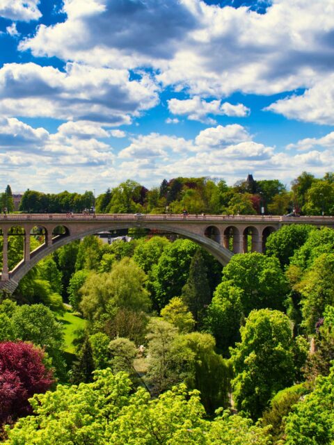 A stone arch bridge, the Pont Adolphe, spans a river gorge in Luxembourg City