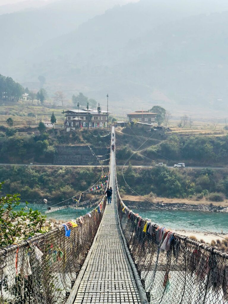 a person walks across a hanging bridge over a river in bhutan