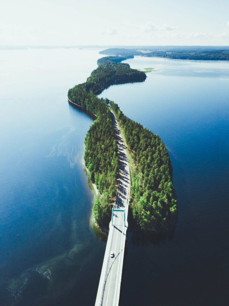 Aerial view of a bridge crossing a narrow strip of land surrounded by calm blue waters under a partly cloudy sky