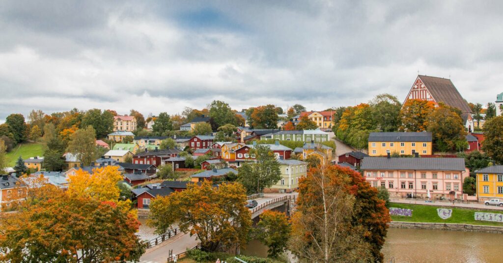 A scenic view of a colorful town with variously colored buildings, surrounded by trees in autumn foliage, under a cloudy sky