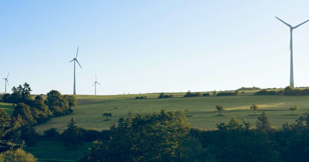 A group of wind turbines with white towers and long, spinning blades stand on a grassy hilltop