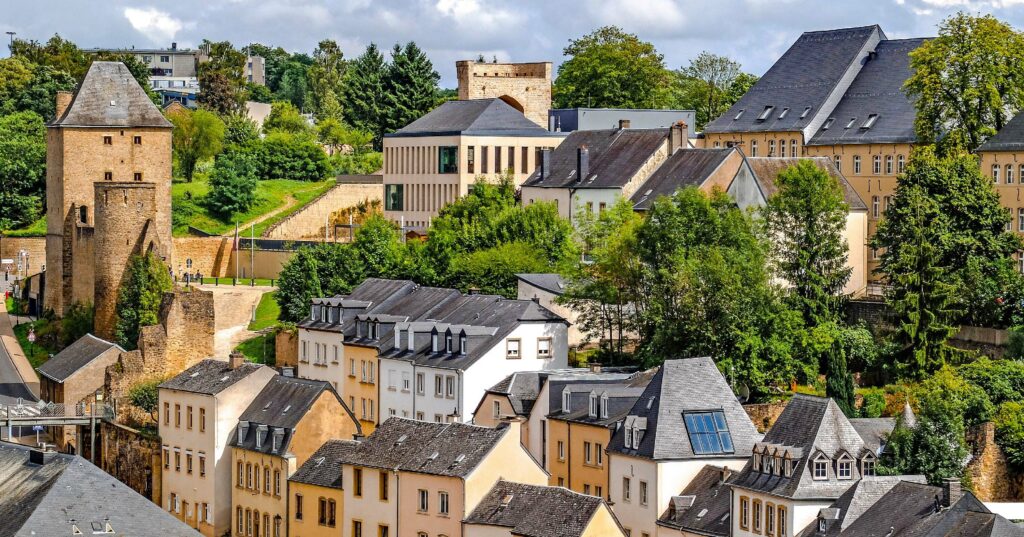 A cluster of colorful houses with red roofs sits on a hilltop, overlooking lush green vegetation