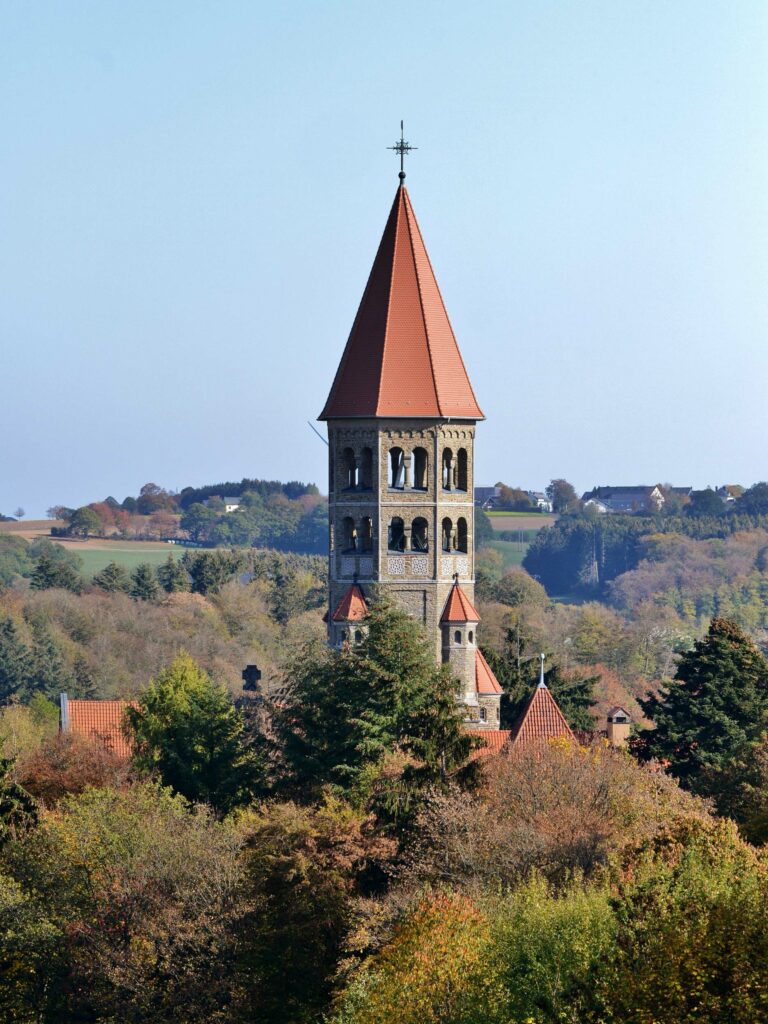 A red-roofed clock tower surrounded by trees, with mountains and rolling hills in the background